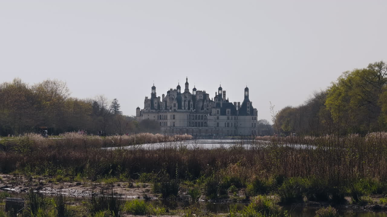 Historic French castle view with river, tourists, and spring nature in Chambord