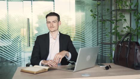 portrait of a handsome, young, stylish man in business attire, sitting at a desk with a laptop in a modern office