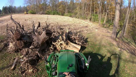 Punto-De-Vista-De-ángulo-Alto-En-Un-Pequeño-Tractor-Verde-Usando-Horquillas-Elevadoras-Para-Recoger-Un-Tocón-De-árbol-De-Una-Pila