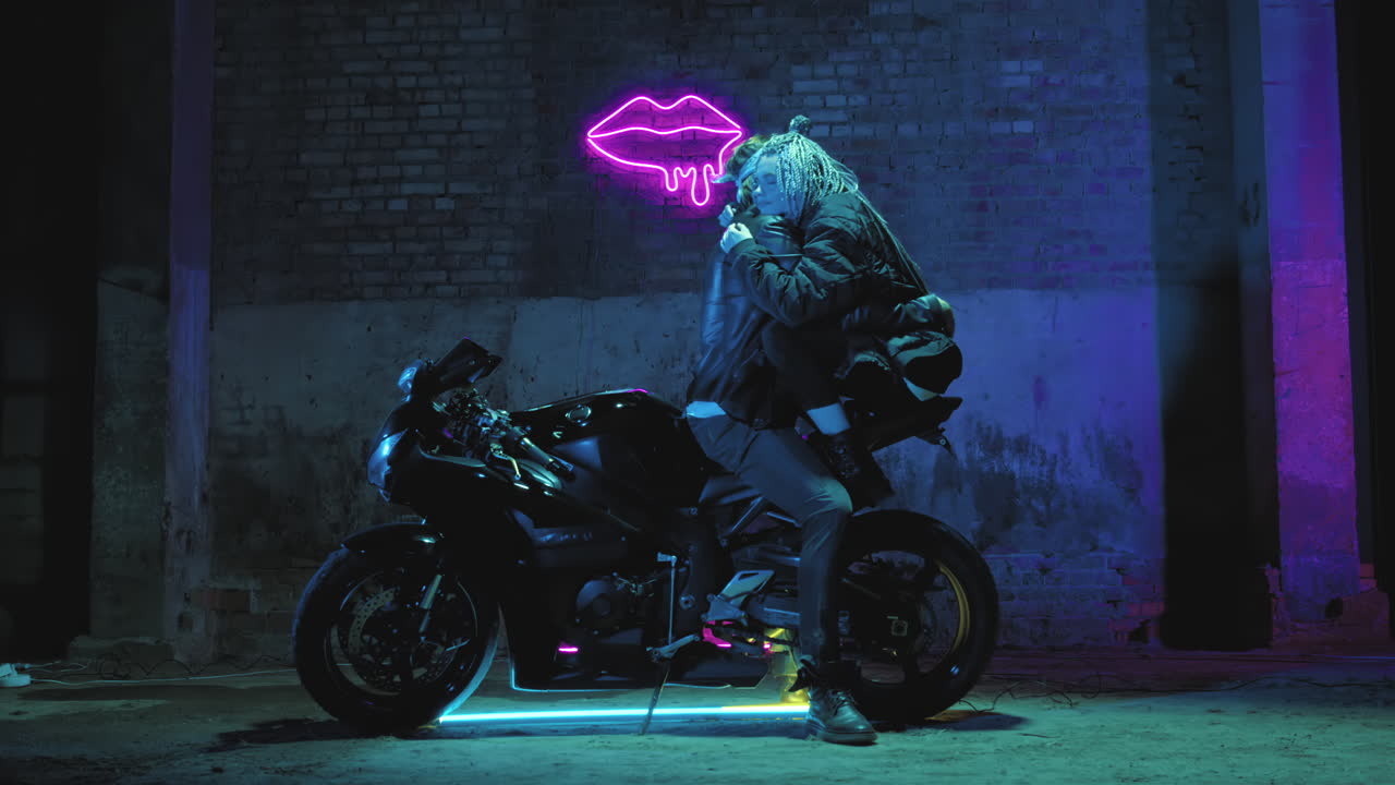 사랑에 빠진 소녀와 한 남자가 슈퍼 스포츠 오토바이에 앉아 유혹하고 포옹하고 있습니다.