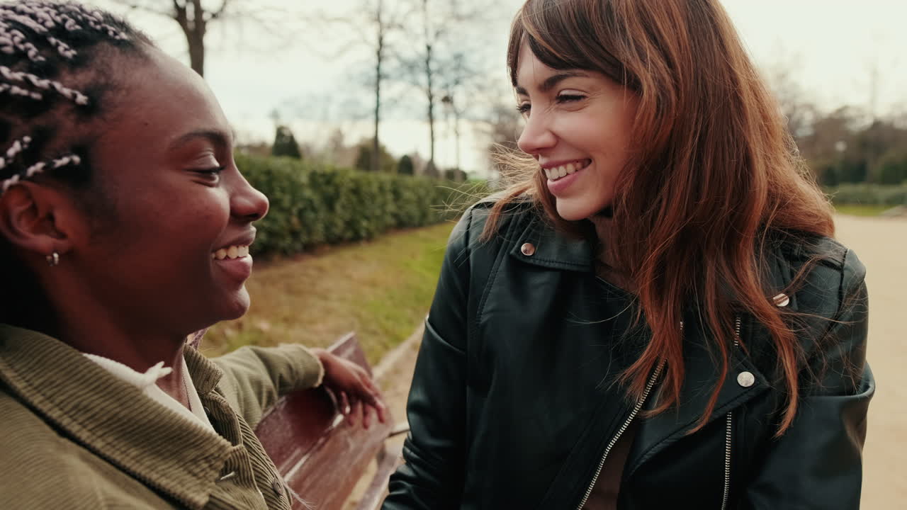 Due giovani donne multietniche sorridenti che parlano su una panchina del parco