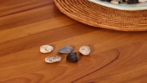 a hand places a black stone among others on a wooden table, creating a balanced arrangement in warm lighting