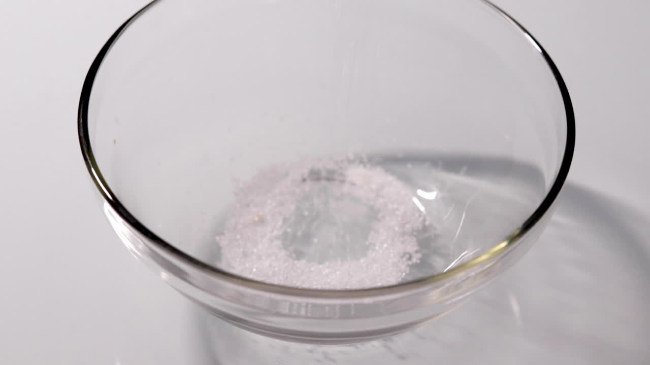 흰색 테이블에 있는 유리 그릇에 설탕을 붓는 슬로우 모션 샷