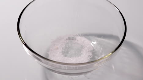 slow motion shot of sugar being poured into a glass bowl on a white table