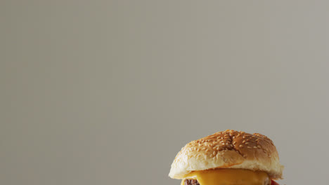 video de primer plano de una hamburguesa con queso con ensalada en un pan de hamburguesa, en un fondo gris pálido con espacio para copiar