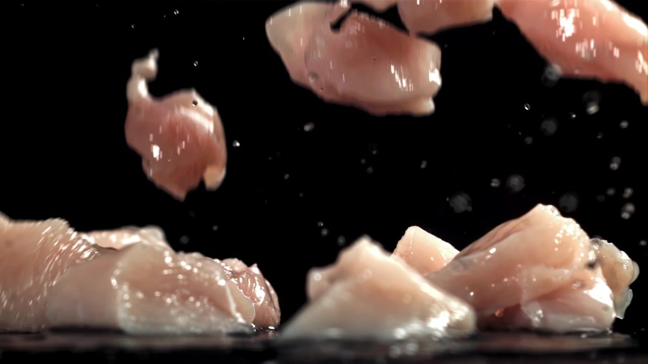 Pezzi di pollo crudo fresco che cadono al rallentatore con schizzi d'acqua