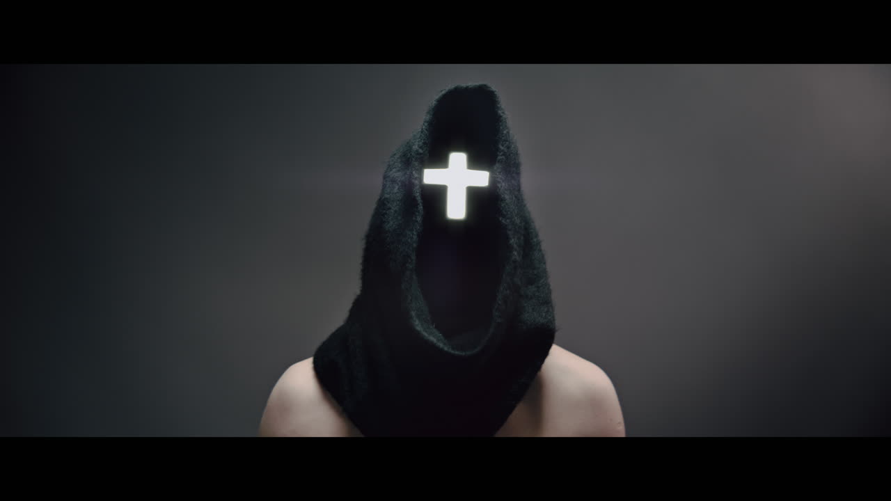 Masked and hooded man with cross of light glowing on his face rise his head