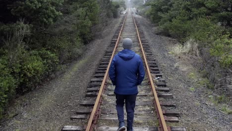 back view of man walking alone on railroad tracks