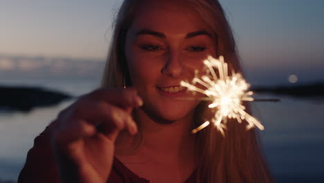 Porträt-Einer-Schönen-Jungen-Blonden-Frau,-Die-Glücklich-Lächelt-Und-Die-Wunderkerze-Anschaut,-Die-Den-Ruhigen-Sonnenuntergang-Am-Strand-Am-Silvesterabend-Feiert