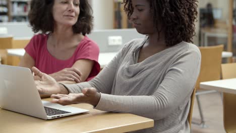 primer plano de mujeres alegres que trabajan con una computadora portátil en la biblioteca