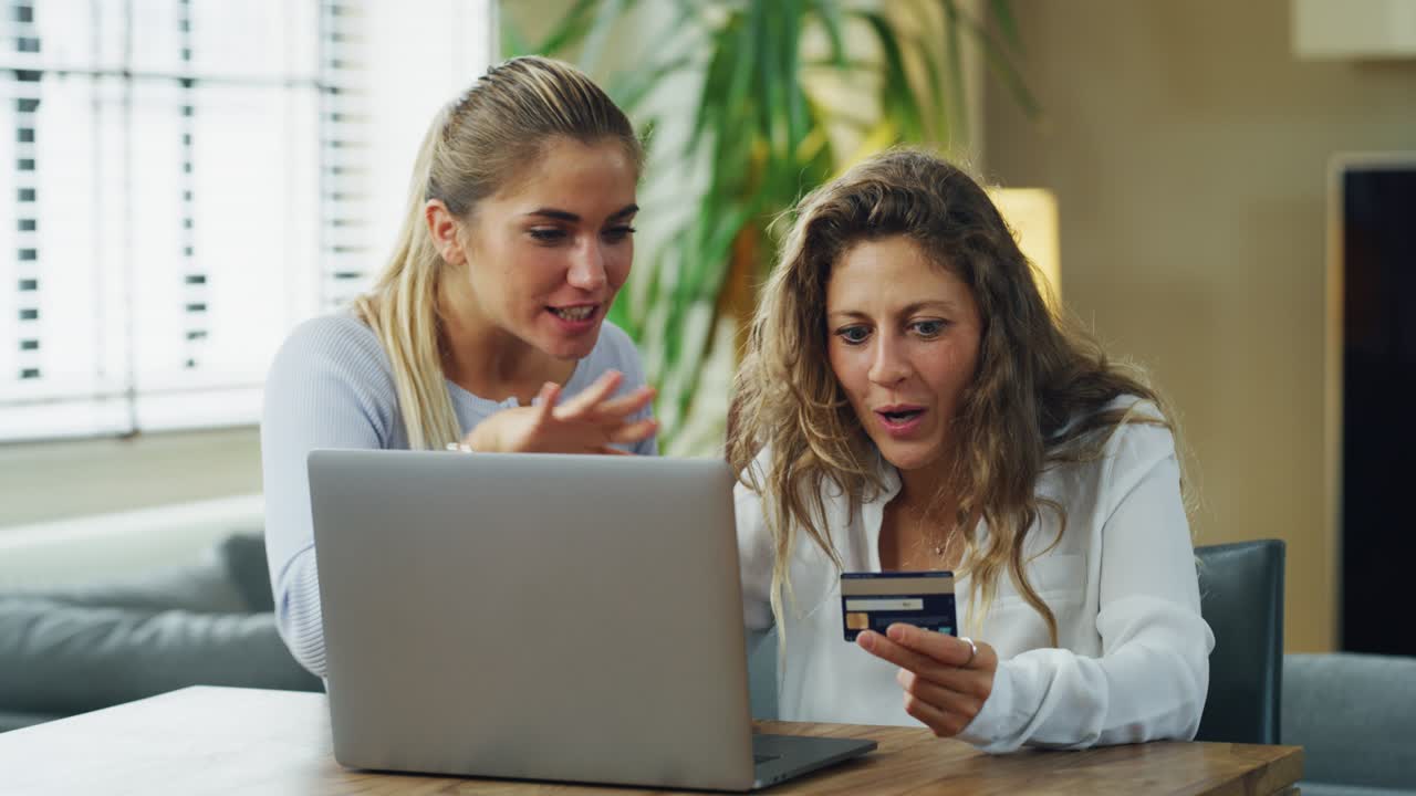 una toma auténtica de amigas jóvenes están ingresando información de tarjetas de crédito usando un teléfono inteligente mientras hacen compras en línea juntas en la sala de estar en casa.