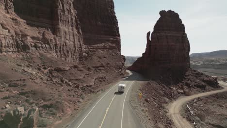 Aus-Der-Luftperspektive-Wird-Ein-Weißer-Wohnwagen-Auf-Seiner-Reise-Durch-Die-öde-Und-Zerklüftete-Landschaft-Von-Utah,-USA,-Verfolgt