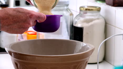 home baker measuring sugar and pouring it into a mixing bowl