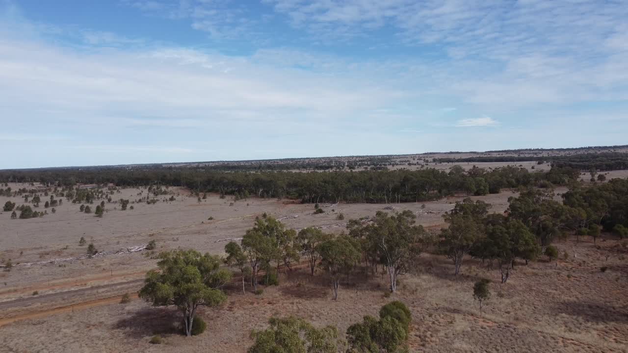 Çöl tarzı bir manzarada demiryolu hattına doğru toprak yolların üzerinde uçan drone.