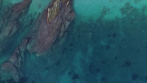 Aerial-drone-shot-captures-the-blue-ocean-waves-crashing-against-the-coastal-rocks-at-Es-Bol-Nou-beach,-showcasing-the-dynamic-interaction-between-sea-and-shore