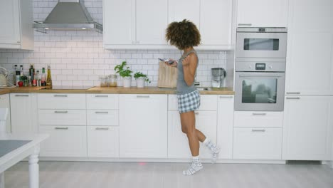 Young-woman-dancing-in-kitchen-with-smartphone