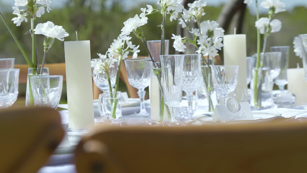 Elegante allestimento del tavolo per il ricevimento di nozze con bicchieri trasparenti, candele e decorazioni floreali. Scatto statico.