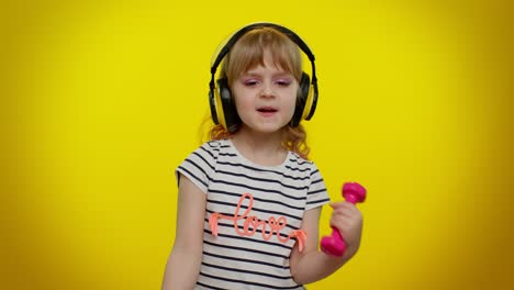 Child-girl-listening-music-via-headphones,-working-out-pumping-up-arm-muscles-lifting-pink-dumbbells