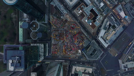 Aerial-birds-eye-overhead-top-down-descending-view-of-machinery-on-construction-site-near-downtown-skyscrapers.-Frankfurt-am-Main,-Germany