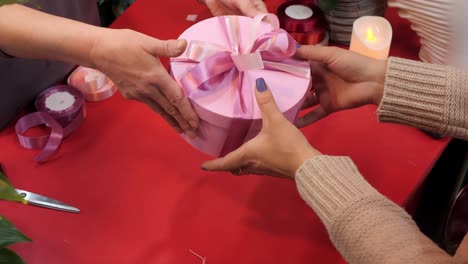 Hands of seller wrapping tapes round pink present box for buyer in shop. Client taking hands round box with pink ribbon in gift shop.