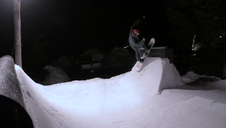 snowboarder masculino haciendo trucos en un parque construido en su patio trasero por la noche