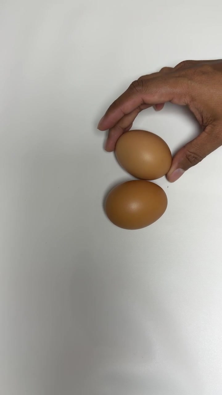Hand Placing Two Brown Eggs on a White Surface