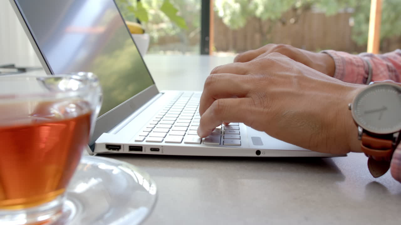 Typing on laptop, man working from home with cup of tea on table