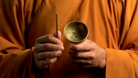 a buddhist monk wearing an orange robe taps a bell with a small stick 1