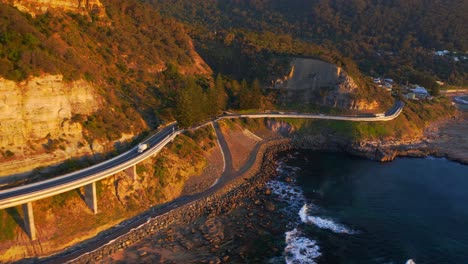 fast forward over curvy sea cliff bridge road, with cars driving in early morning, nsw australia - aerial shot