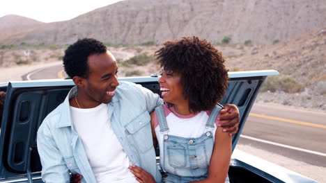 laughing couple sitting on car at roadside stop on road trip
