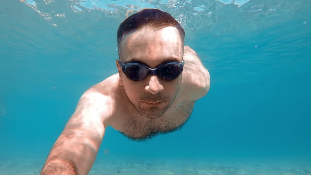 Uomo con occhialini da nuoto sott'acqua che tiene in mano una fotocamera, Mar Egeo. Rallentatore, riprese subacquee. Grecia