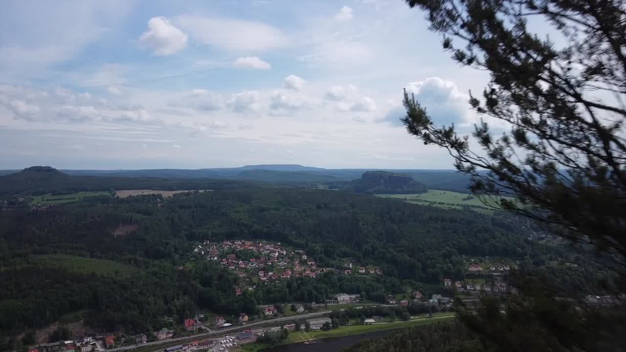 Drone footage from up above on a mountain flying between tress into the great wide open with view of a valley and fields and clouds in eastern Saxony Germany