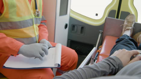 close up view of a patient lying on a stretcher inside an ambulance while a paramedic taking notes in medical report