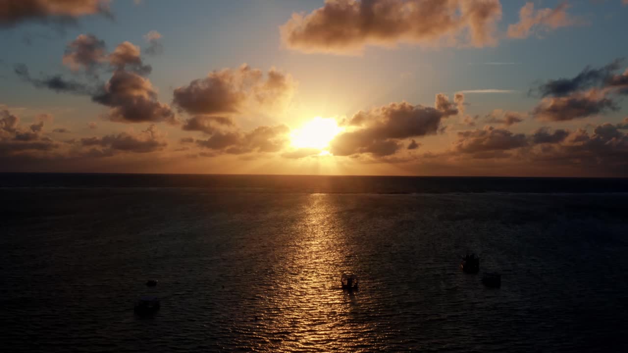 Smukt luftfoto fra drone af en havsolopgang ved Well Beach nær João Pessoa en varm sommermorgen med vandet nedenfor, gyldne skyer på horisonten og små både i vandet.