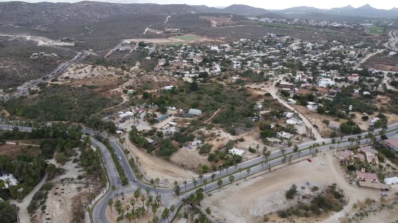 vista aérea frente a la zona costera de la marina puerto los cabos con una vista de un asentamiento con edificios coloridos, paisaje seco y la marina con barcos en la orilla