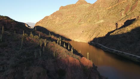 Antena-De-4k-De-Un-Dron-Volando-Sobre-Un-Río-En-El-Desierto-Durante-La-Hora-Dorada-Que-Muestra-Cactus,-Montañas-Y-Parte-De-Un-Cielo-Azul,-Río-Salado-En-El-Lago-Roosevelt-Arizona,-Sendero-Apache