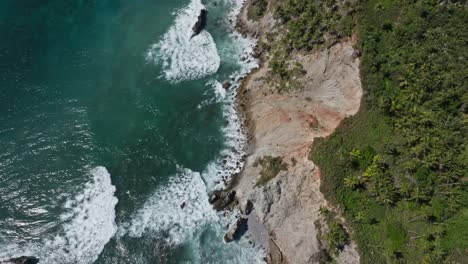 Weite-Schwenkaufnahme-Von-Felsigen-Meeresklippen-Mit-Palmen-Und-Vegetation-Und-Einem-Türkisfarbenen-Wasser-Und-Wellen