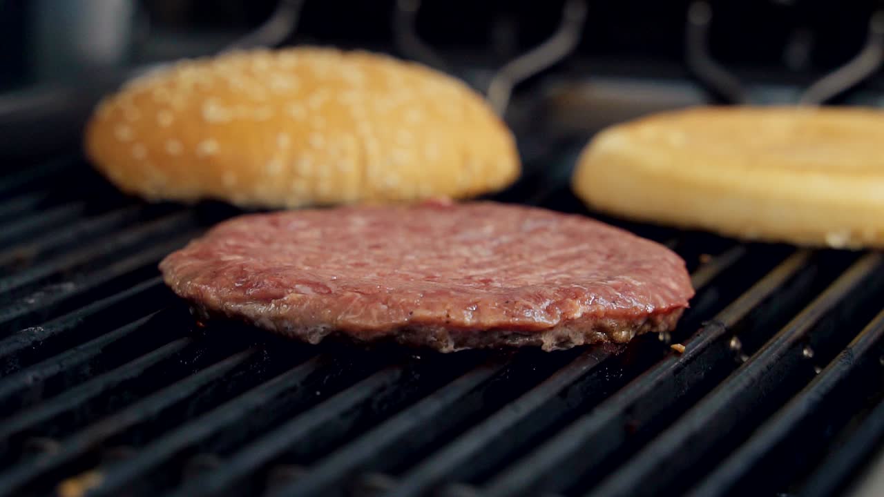 Cooking meat cutlet and buns on hot grill. Process of frying tasty components for burger. Beef cutlet frying in fast food restaurant. Close-up