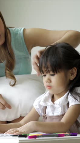 a young, asian child work and play at home with her mother learning to read and write in the cozy comfort of their living room