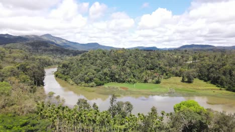 Aerial-backwards-shot-of-dirty-River-surrounded-by-jungle,mangroves-and-mountain-range-in-background---Kerela,India