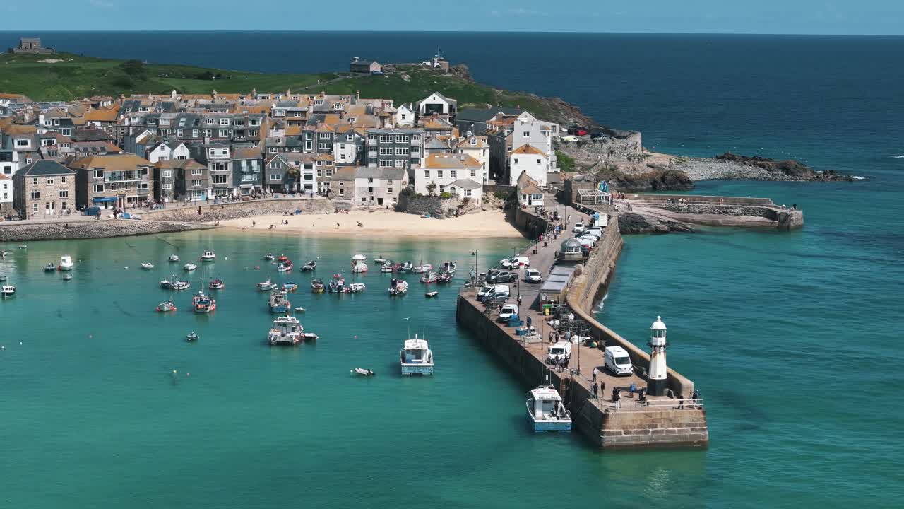 Low drone orbit around St. Ives harbor at coast level with boats and rooftops visible, bustling waters