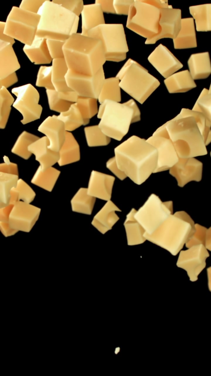 Movimento rallentato di cubetti di formaggio che cadono su sfondo nero