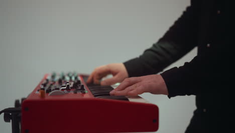 close-up of hands playing on a red sampler, set against a softly blurred background in a serene studio