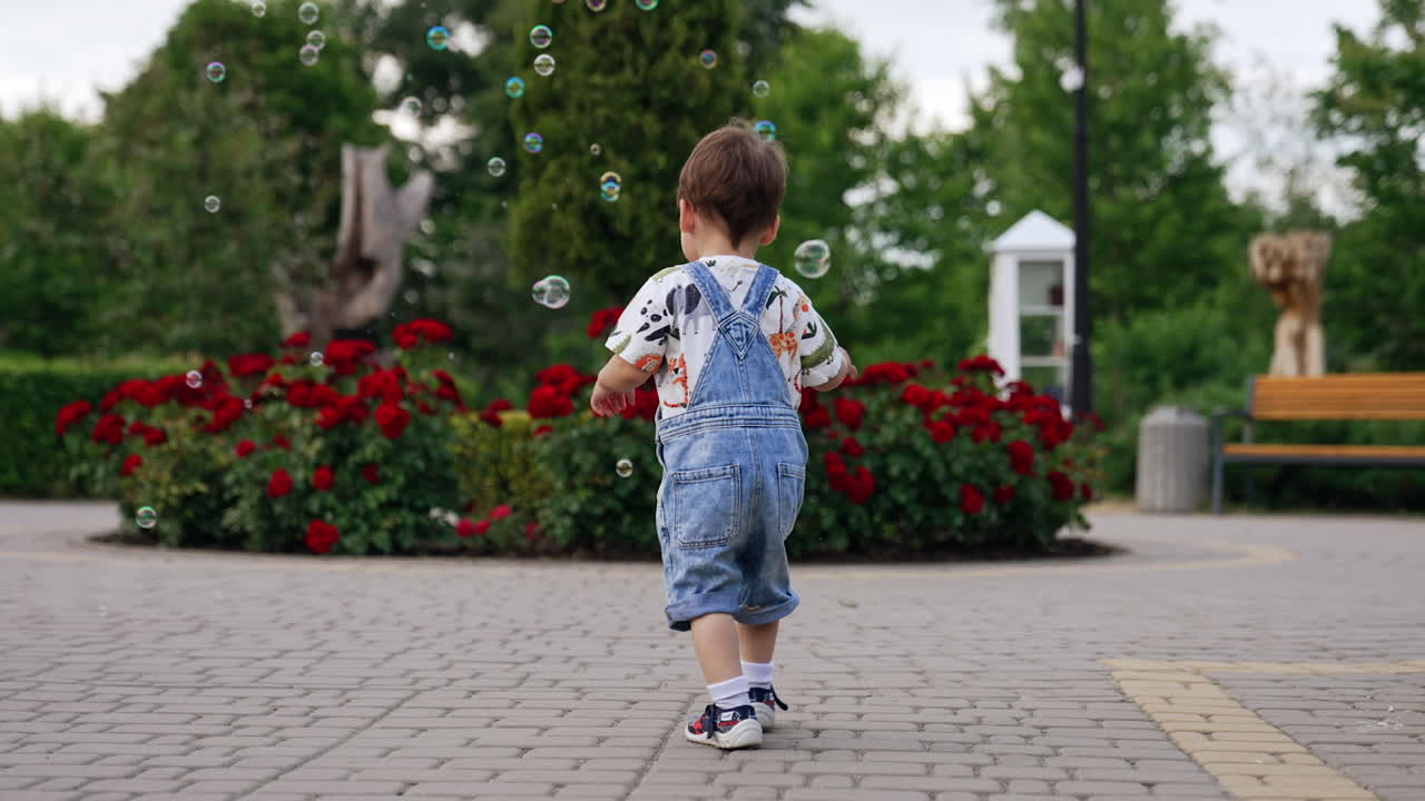 Adorable toddler in a jeans romper playing with soap bubbles. Happy kid playing in the park in summer.