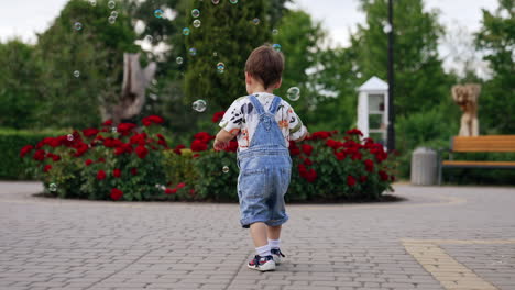 adorable toddler in a jeans romper playing with soap bubbles. happy kid playing in the park in summer.