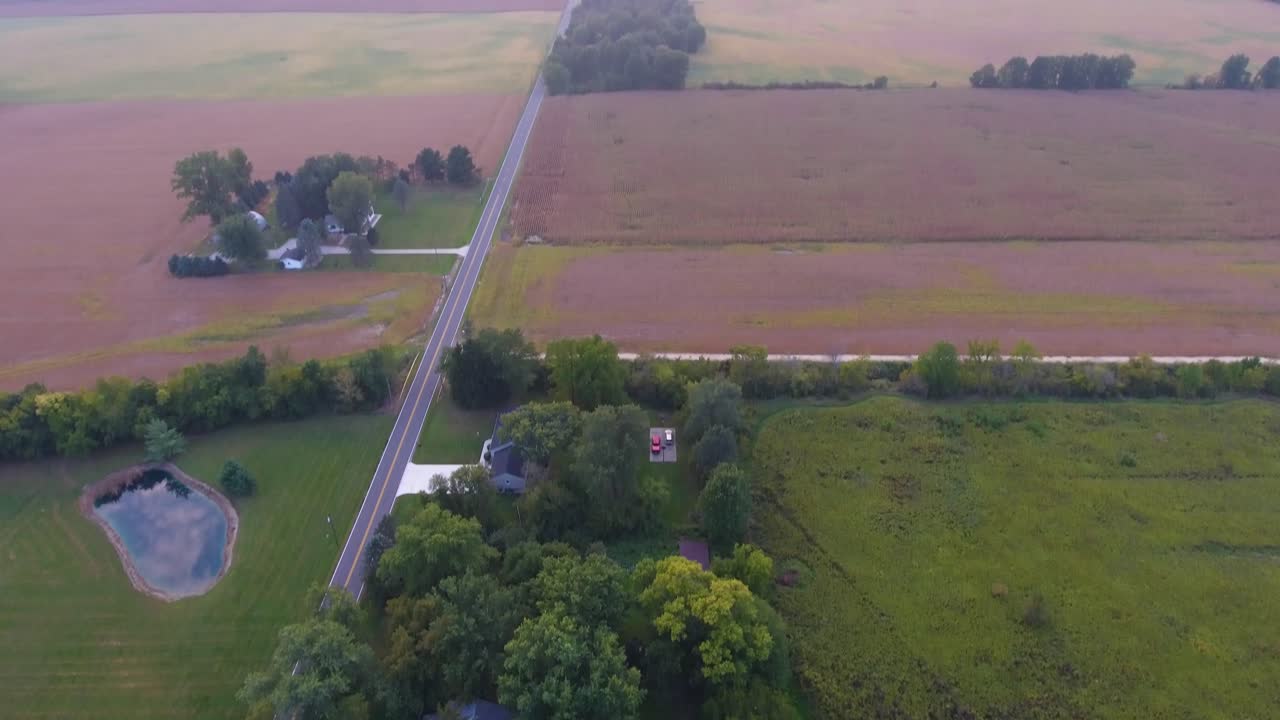 Aerial view a house with a swimming pool in the country with fields surrounding it following the path of the road in 4K