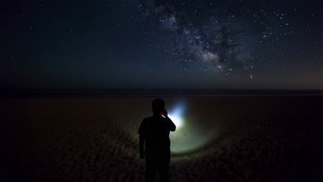 person with flashlight on a beach under the milky way night sky