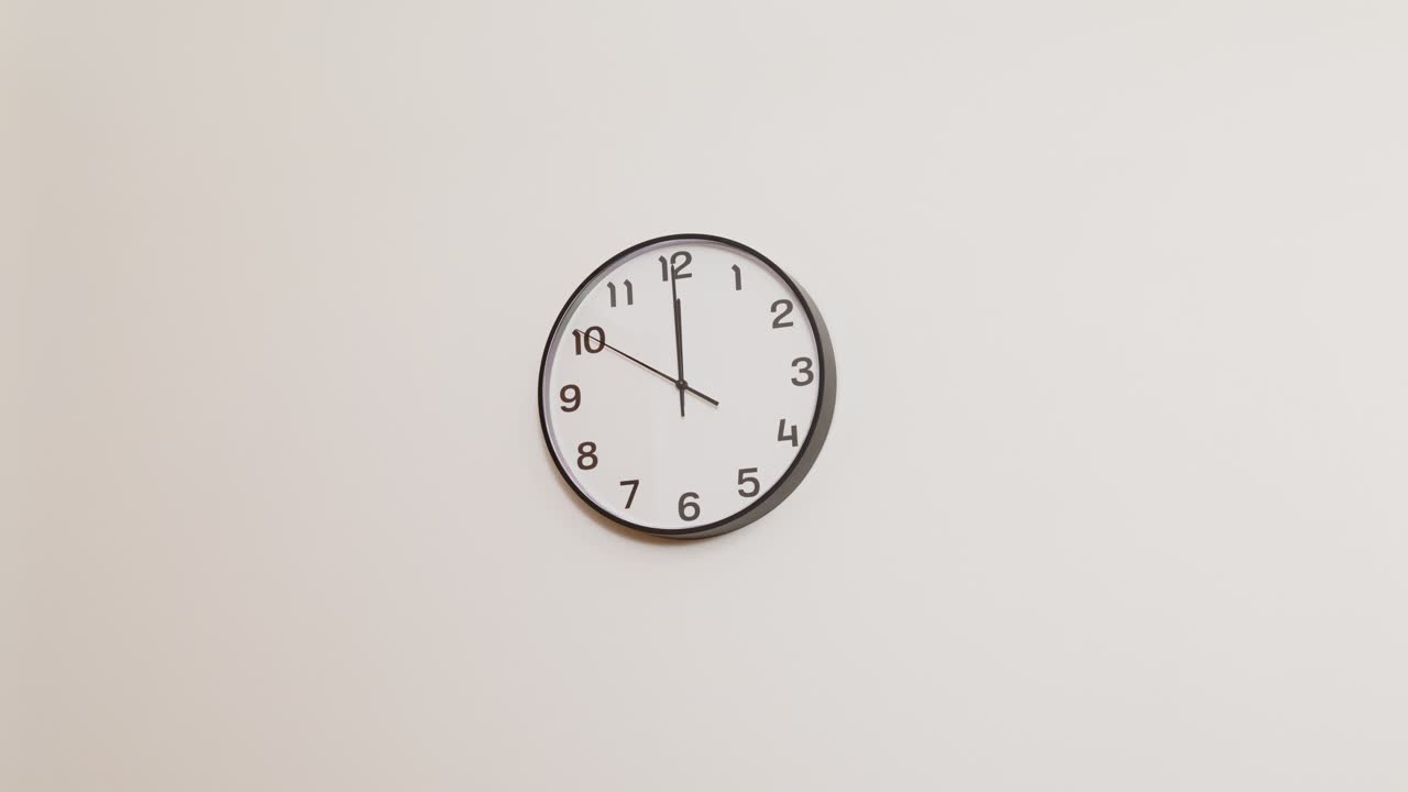A traditional office wall clock with bold black numerals and a clear white background, marking the time at 12:00.