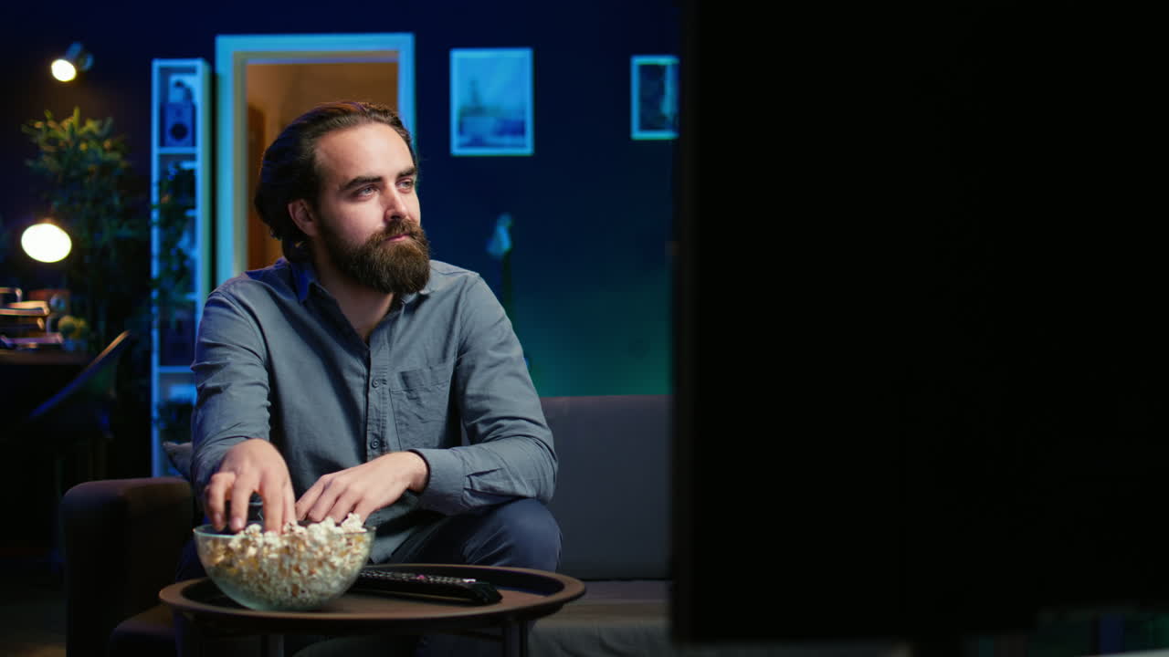 가정 에서 소파 에 앉아 있는 남자 는 텔레비전 스크린 에서 보여지는 흥미진진 한 영화 를 지켜보고 있다