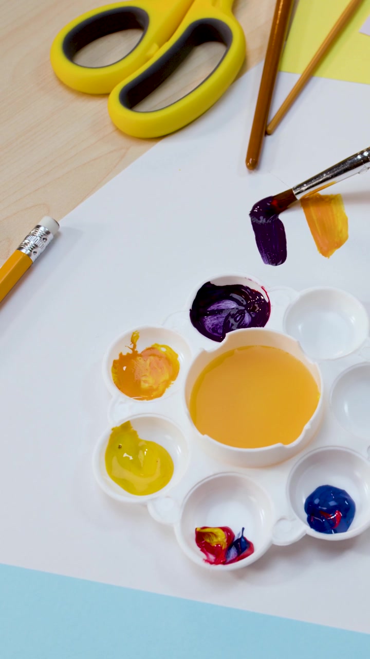 Primo piano dall'alto di un artista che mescola pittura viola e applica pennellate su carta bianca.